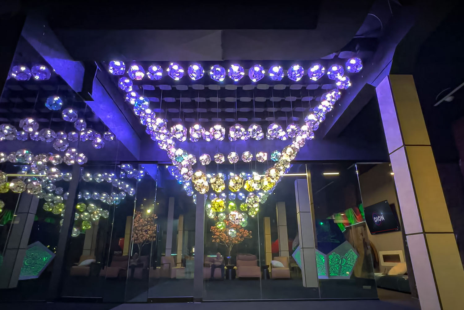 Kinetic light installation in SKYFORM STUDIO showroom, ceiling structure with glowing crystal-like spheres creating colorful reflections.