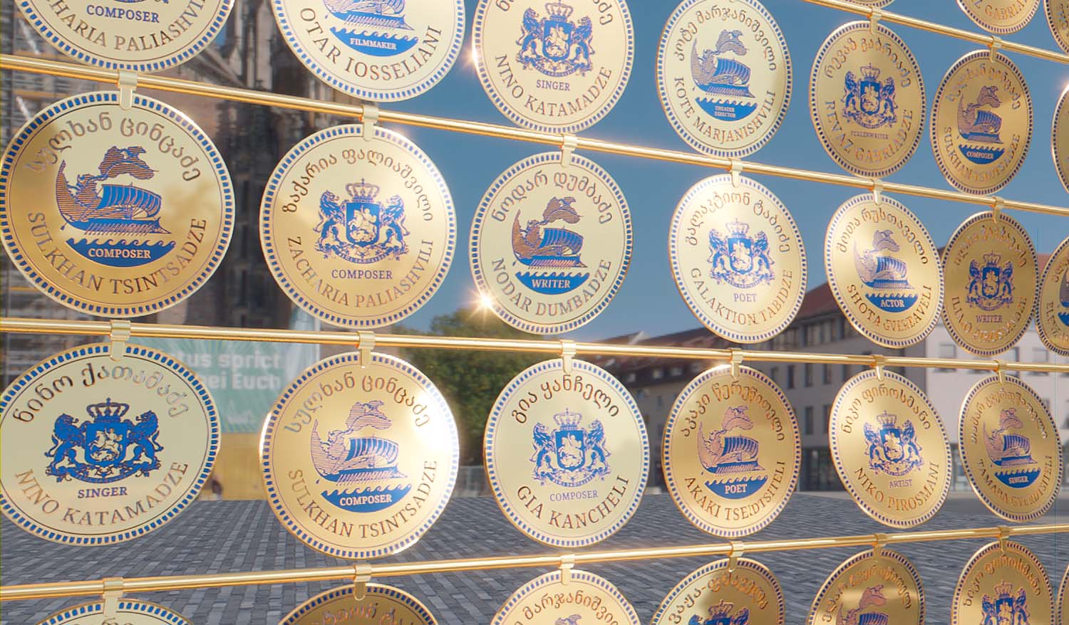 Крупный план инсталляции из круглых позолоченных монет с именами выдающихся жителей Грузии и декоративной символикой, создающих ритмичный визуальный узор.