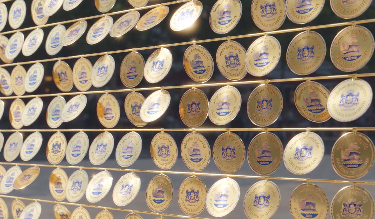 Золотые диски с гравировкой и эмблемами, размещённые в несколько рядов, формируют светящуюся публичную композицию под открытым небом.