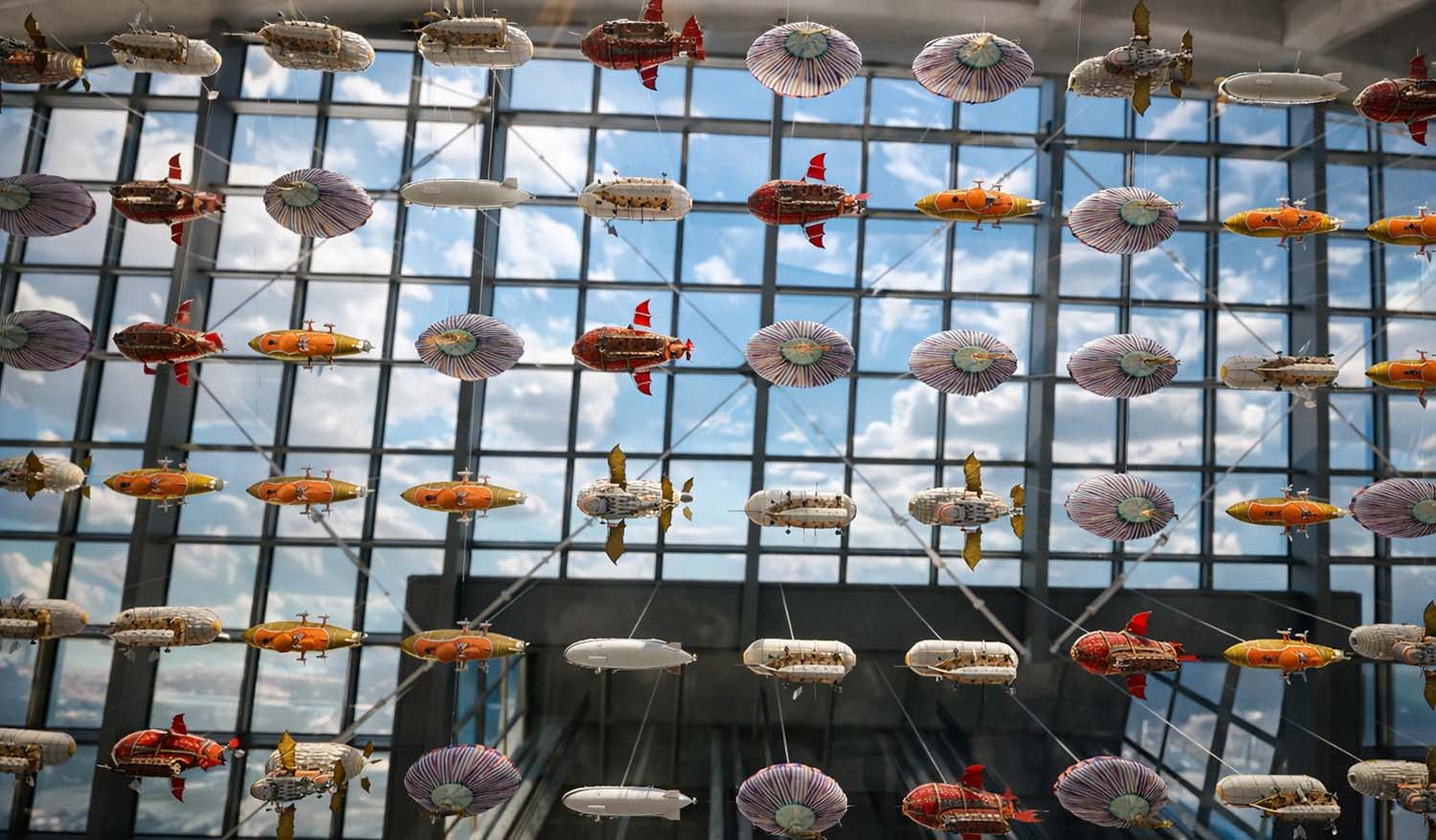 Стимпанк-дирижабли разных форм и размеров парят в пространстве аэропорта, формируя масштабную кинетическую арт-инсталляцию.