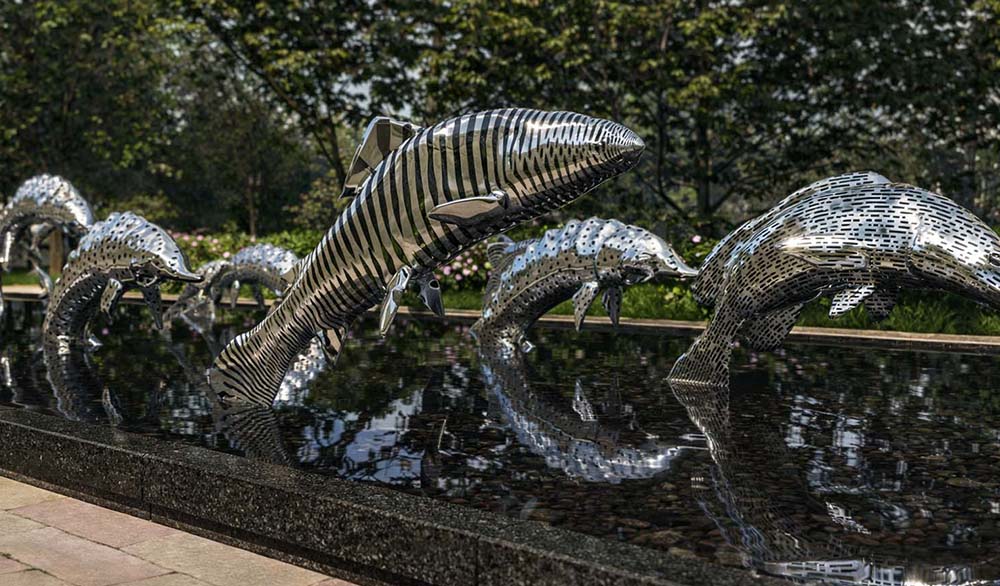 Металлические скульптуры рыб в проекте «Водный мир» с полосатой и перфорированной текстурой, отражающиеся в тёмной глади воды парка.