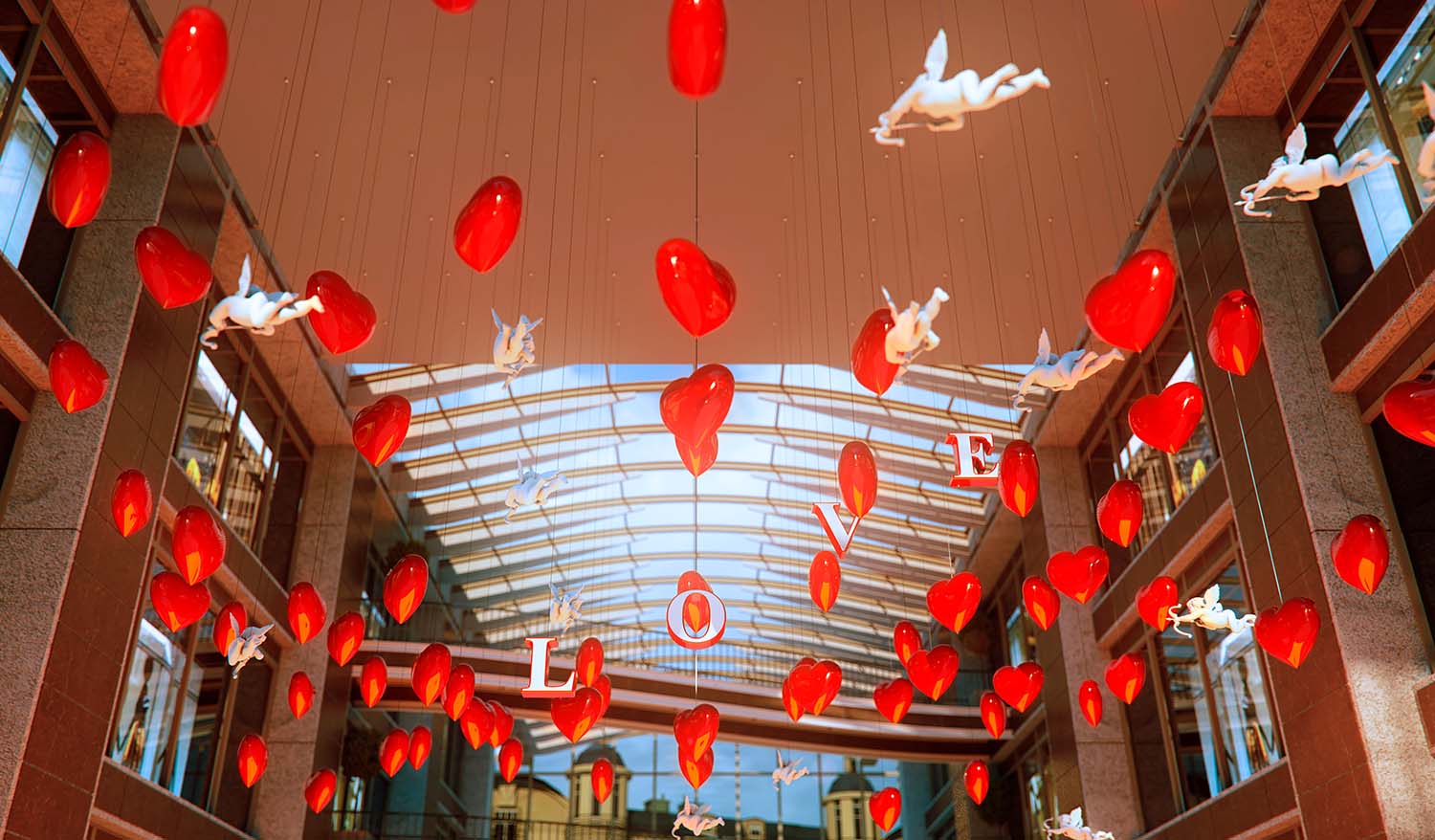 Кинетическая инсталляция в атриуме торгового центра — подвешенные красные сердца и белые фигуры купидонов формируют воздушную композицию, а объёмные буквы LOVE создают романтическую атмосферу под стеклянной крышей.