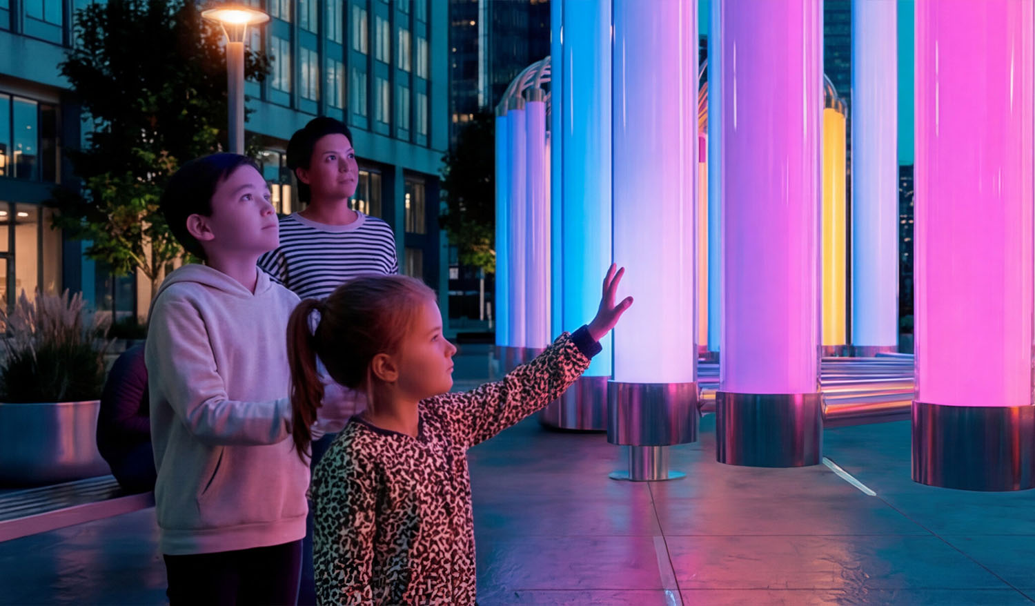 Интерактивная инсталляция «Пульс Света» в городской среде: дети взаимодействуют с высокими светящимися поликарбонатными трубами, касаясь их и вызывая мягкие пульсирующие цветовые переходы (розовый, голубой, фиолетовый), формирующие живое световое пространство вечером