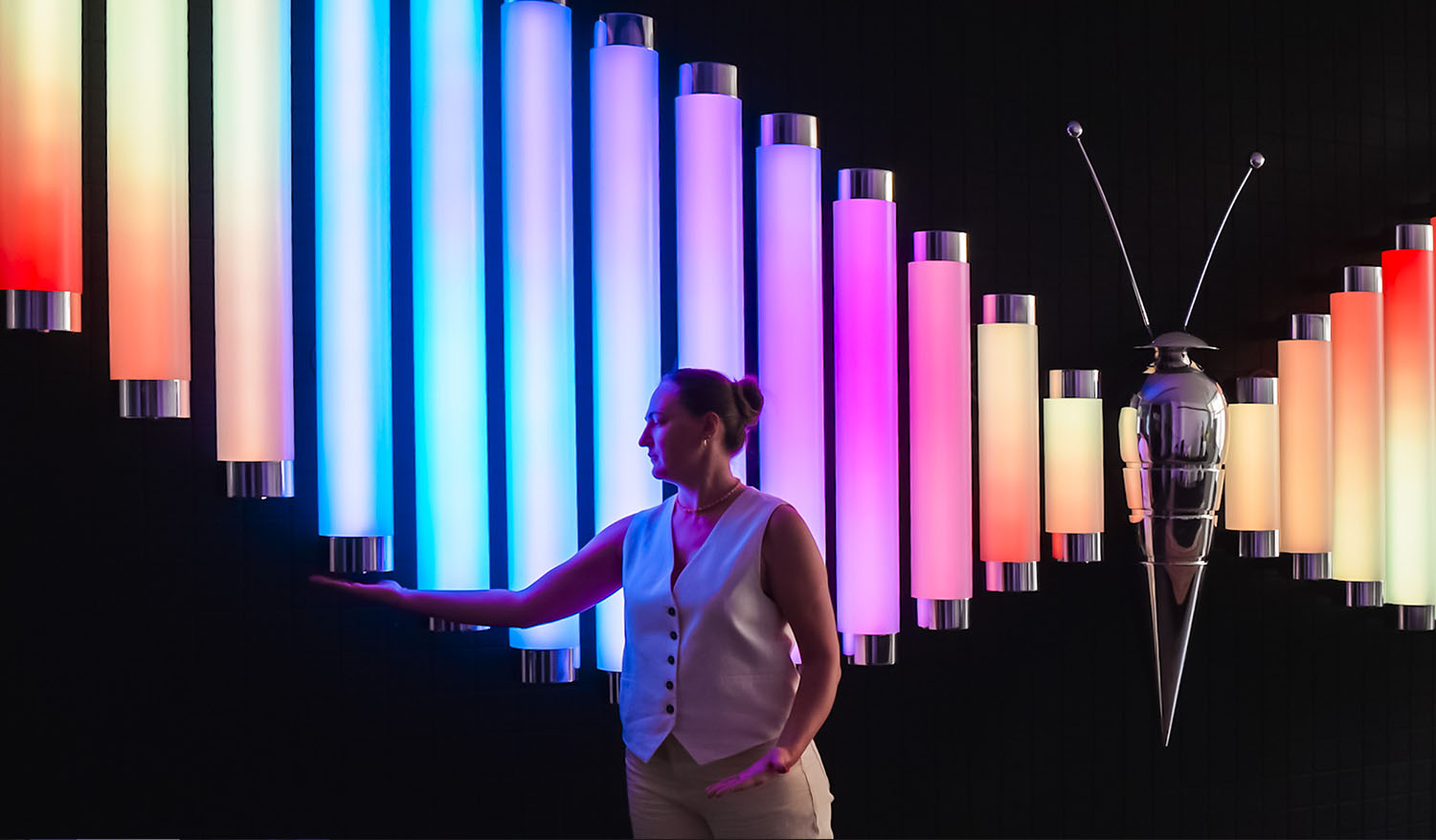 Visitor interacting with the Butterfly installation featuring colorful illuminated tubes and a metallic butterfly sculpture.