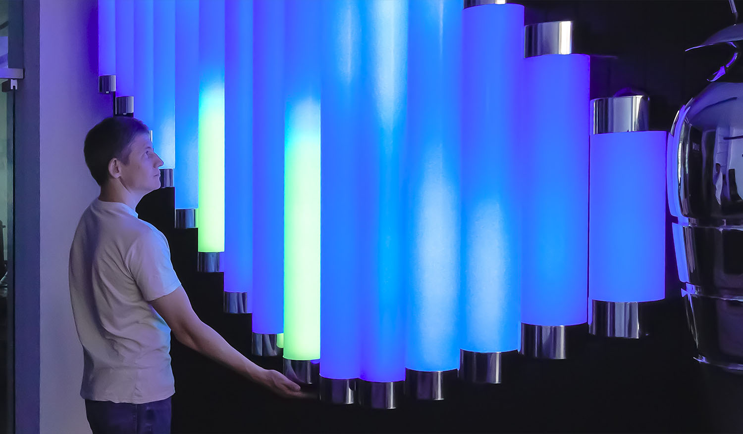 Visitor interacting with the Butterfly installation by touching glowing blue, turquoise, and green light tubes.